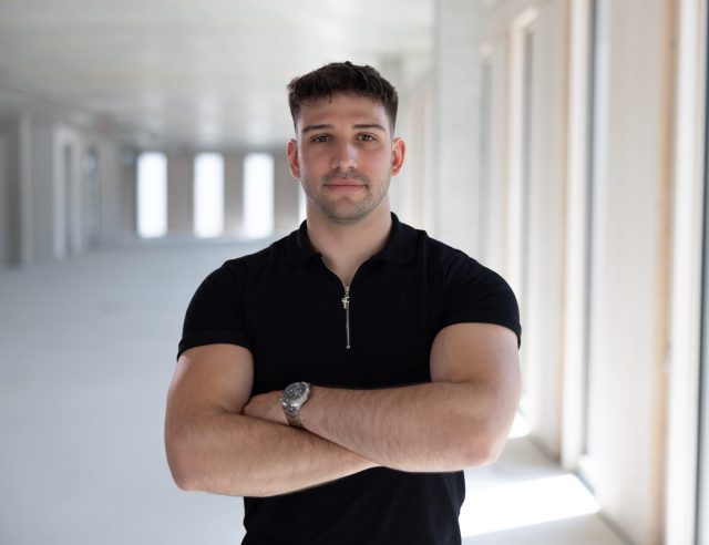 The picture shows Robin Nemetz, Business Unit Director of PCG DACH x Development. He is standing facing the viewer, his arms crossed, wearing a black T-shirt.