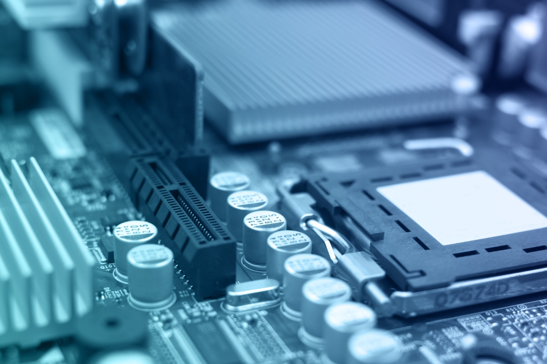 A close-up, blue-tinted photo of a complex computer circuit board (motherboard) with various components, including capacitors, slots, and a heat sink, representing the physical hardware being consolidated and the legacy systems that contribute to technical debt.