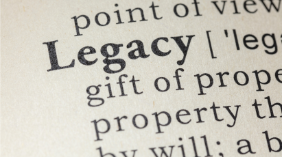 A close-up photograph of a dictionary page, with the word "Legacy" clearly highlighted in bold black font, followed by its phonetic transcription and part of the definition.
