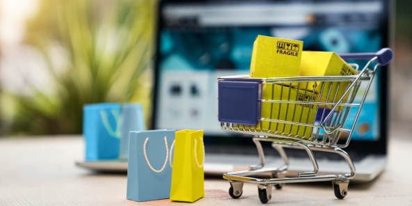 The image shows a shopping cart with packages in front of a laptop. The Public Cloud Group (PCG) optimizes e-commerce cloud solutions.