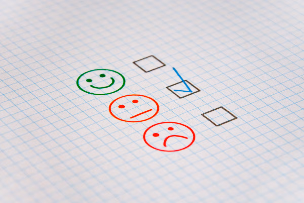 Checkered paper with a checklist. It shows a smiling, a neutral, and a sad smiley face. The checkbox next to the neutral smiley face is checked.